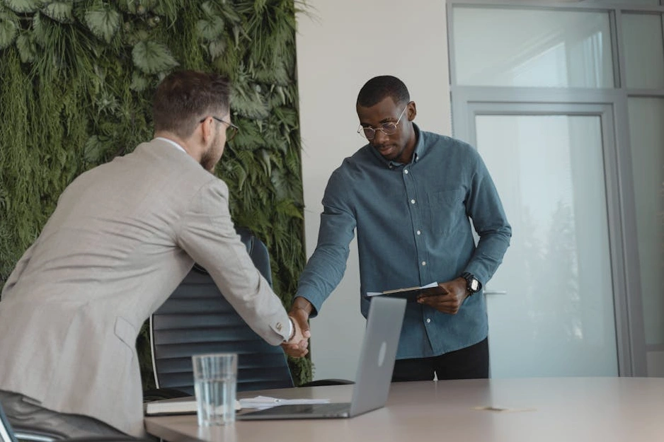 Dwie osoby podające sobie ręce na tle panoramy miasta, symbolizujące partnerstwo biznesowe.
